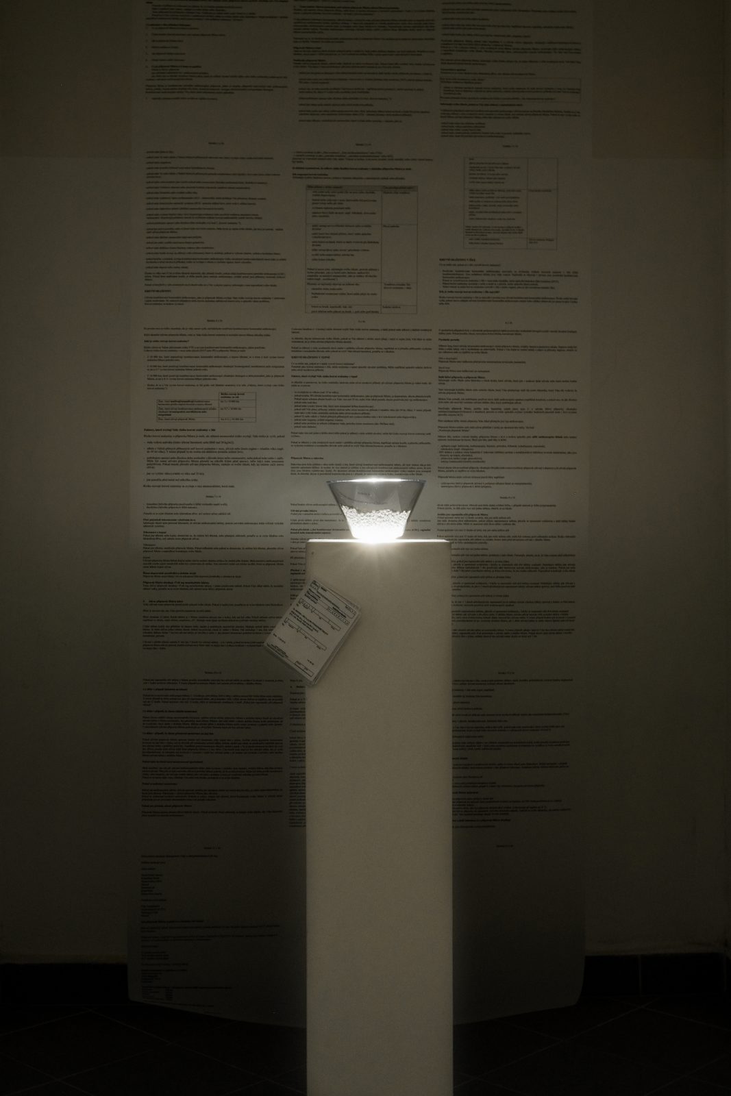 The lit bowl on its plinth in front of the enlarged package insert