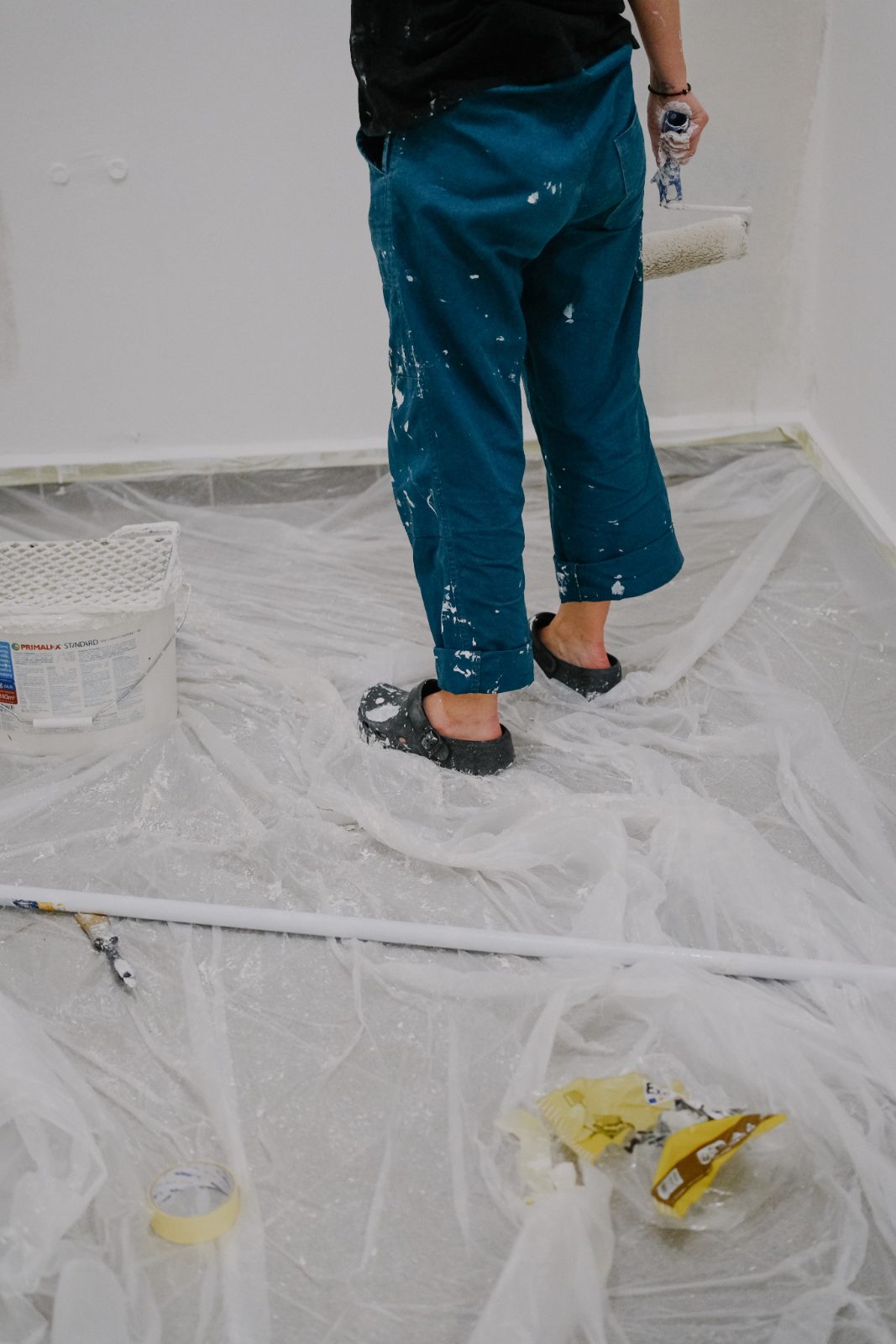 Paint-splattered trousers and shoes on a plastic-covered floor