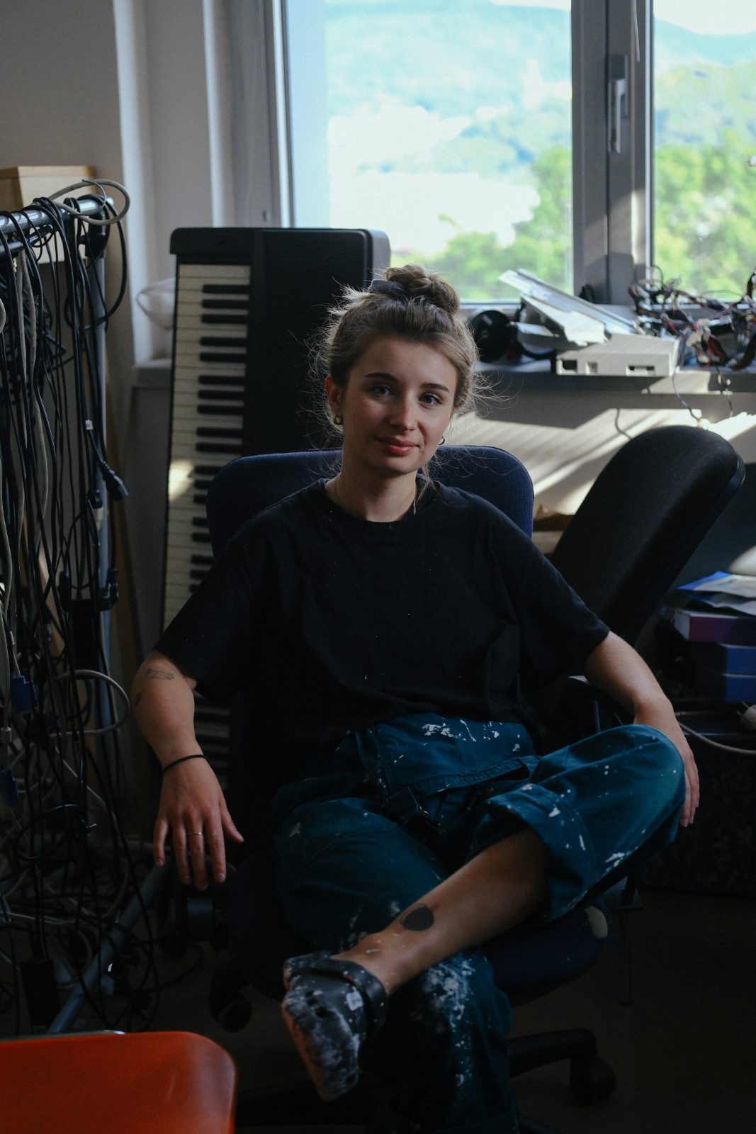 Natálie Sedláčková sitting on an office chair in her studio, surrounded by cables and equipment