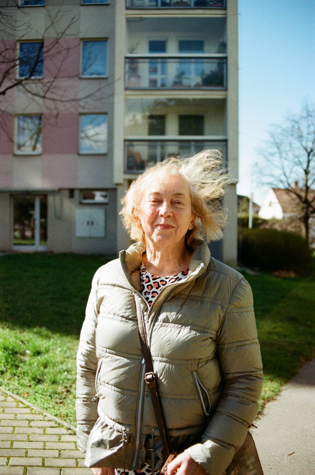 Older woman with windswept hair in front of a housing block