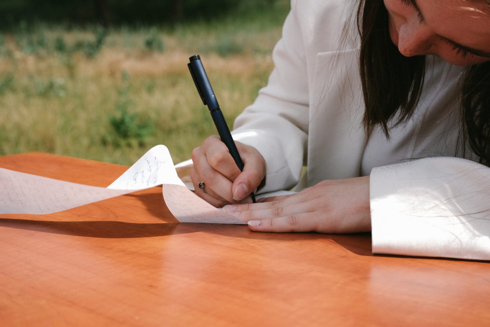 Hand signing a long paper scroll on a wooden table in a meadow
