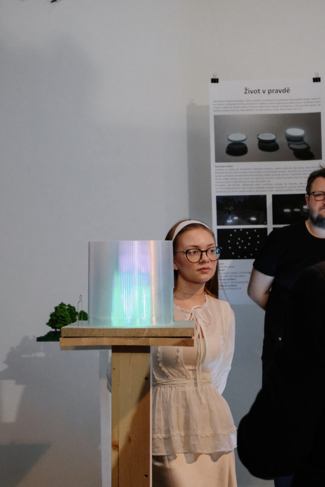 A woman standing beside a glowing light object on a wooden stand