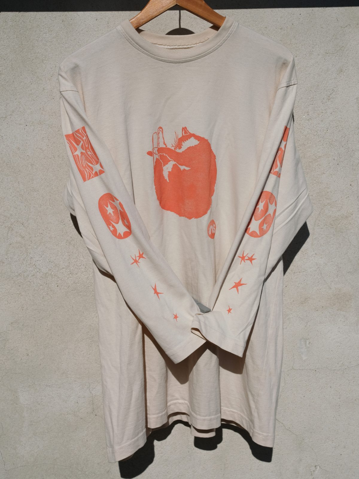 Cream long-sleeve shirt with an orange curled-up cat print and star motifs on the sleeves