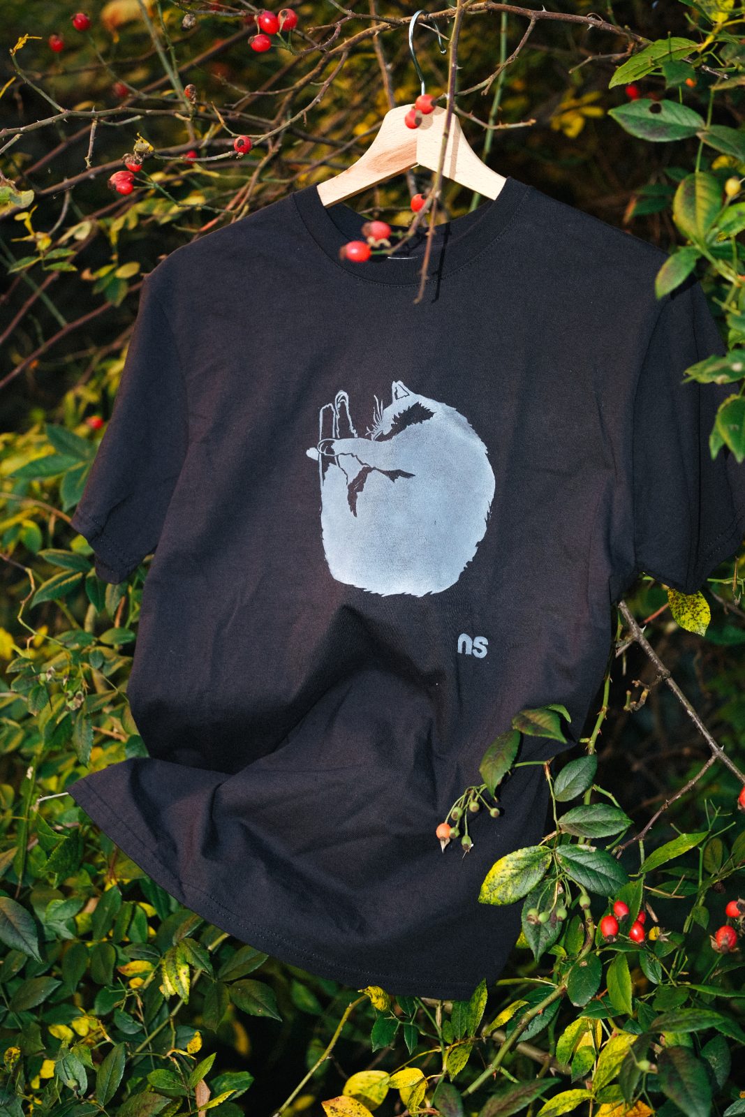Hand-printed black T-shirt hanging among green leaves