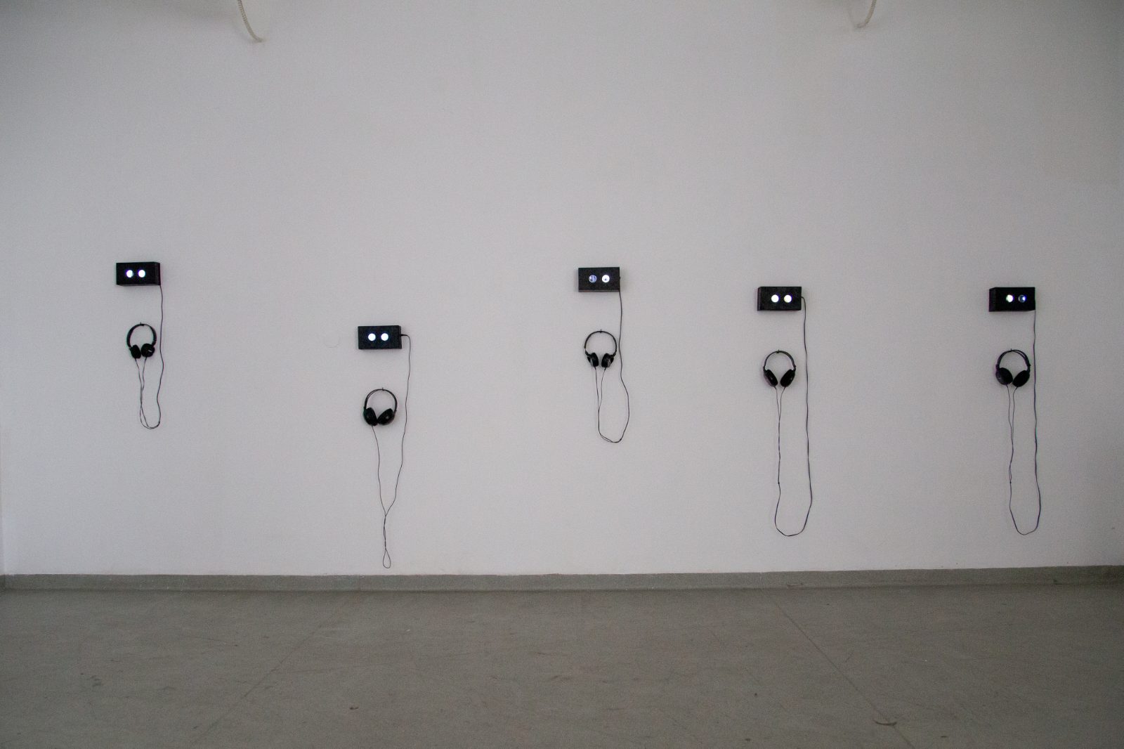 Five small screens with headphones hanging in a row on a white wall